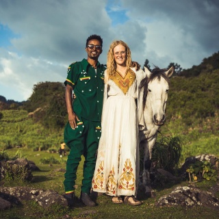 Valerie und ihre Mann Abiy stehen Arm in Arm zusammen mit ihrem Pferd in einem grünen Tal.