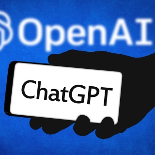 Die Silhouette einer Hand hält ein Smartphone mit der Aufschrift "ChatGPT". Im Hintergrund leuchtet das OpenAI-Logo auf einem blauen Hintergrund.