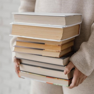 Frauenhände halten eine Stapel voller Bücher.