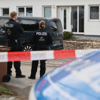 Polizisten stehen an einer Flatterbandabsperrung vor einem Tatort.