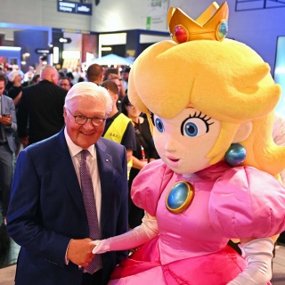 27.08.2026, Nordrhein-Westfalen, Köln: Bundespräsident Frank-Walter Steinmeier wird bei einem Rundgang über die Gamescom am Nintendo-Messestand von Prinzessin Peach begrüßt, einer Figur aus der Super-Mario-Reihe. Steinmeier ließ sich an dem Stand ein...