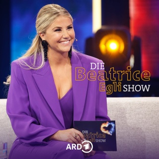 Beatrice Egli auf der Couch ihrer Show, lächelnd, mit Mikro – daneben der Schriftzug ihrer Show
