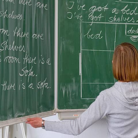 ARCHIV - ILLUSTRATION - Eine Englisch-Lehrerin schreibt  in einer Grundschule an die Tafel.