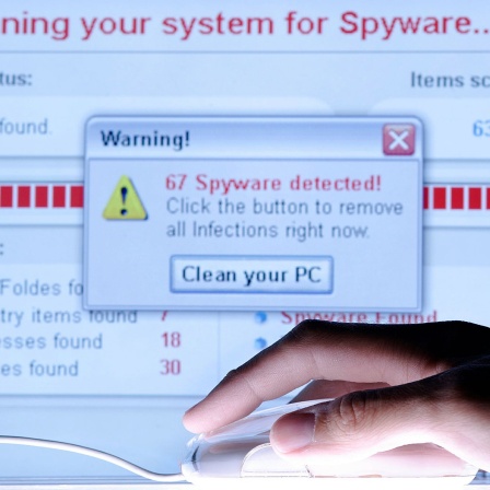 Eine Hand auf einer Maus vor einem Computermonitor, auf dem eine Virenwarnung angezeigt wird