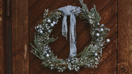 Adventstürkranz aus Tannenzweigen mit Perlen besetzt, an einer braunen Holztüre.