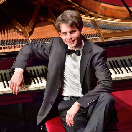 Der Organist und Pianist Markus Schmidt aus nahezu Vogelperspektive, am offenen Flügel sitzend – junger Mann mit Sakko, Hemd und Fliege
