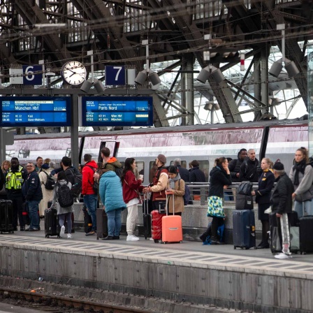 Bahnreisende warten auf dem Bahnsteig auf die Einfahrt eines Zuges im Kölner Hauptbahnhof.