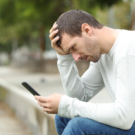 Ein trauriger erwachsener Mann liest schlechte Nachrichten auf dem Smartphone.