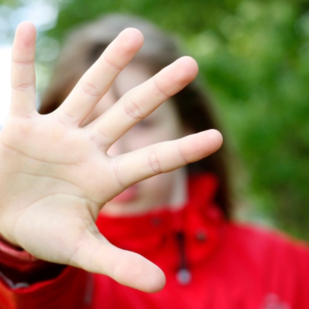 Mädchen hält abwehrend Hand vors Gesicht