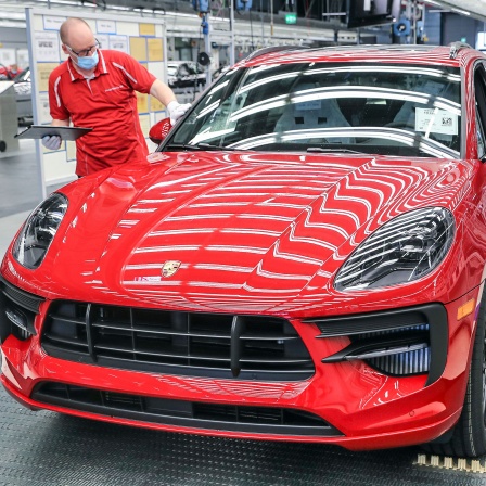 Ein Mitarbeiter von Porsche führt mit Mundschutz die finale Qualitätskontrolle an einem Macan durch, bevor dieser vom Band rollt.