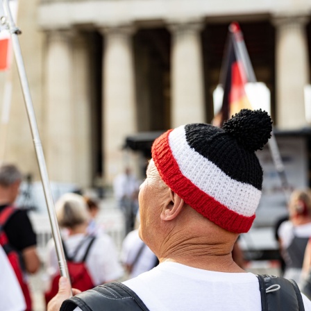 Reichsbürger demonstrieren am 31.08.2024 in München. Mann im Vordergrund trägt eine schwarz-weiß-rote Strickmütze.