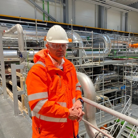 Der Bürgermeister von Esbjerg, Jesper Frost Rasmussen, steht mit Sicherheitshelm in einer Halle der Meerwasser-Wärmepumpe.