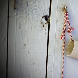 Eine leere Rolle Toilettenpapier hängt an einem rot-weißen Band an einer Bretterwand.