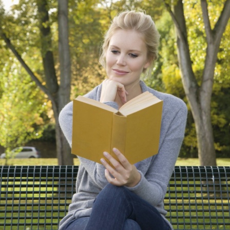 Symbolbild: Eine Frau sitzt auf einer Bank und liest ein Buch