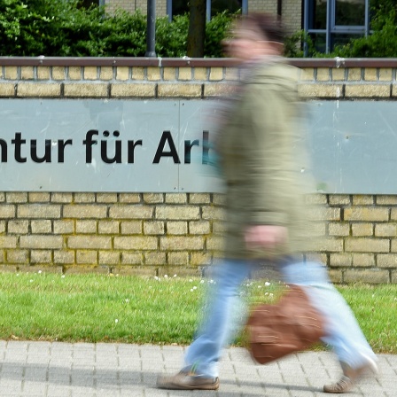 Eine Frau läuft an einem Schild mit der Aufschrift "Agentur für Arbeit" vorbei.