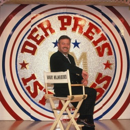 Harry Wijnvoord sitzt 1993 in seiner RTL Game-Show "Der Preis ist heiß" vor dem Logo auf einem Regiestuhl.