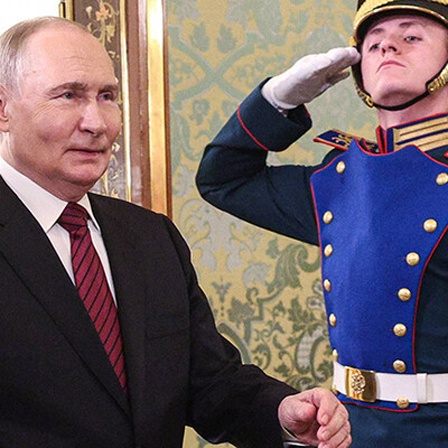 Putin schreitet von links nach rechts, im Hintergrund steht ein salutierender Soldat.