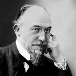 Erik Satie, der Komponist trägt eine Brille und einen Ziegenbart.