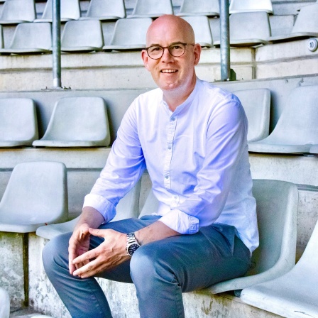 Alexander Jacob sitzt auf einem Tribünenplatz in einem Fußballstadion. Alexander Jacob litt jahrelang unter Wettsucht und klärt heute über Sportwetten und Spielsucht auf.