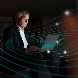 Ein Mann sitzt an seinem Laptop. Mit einem Grafikprogramm erstellte Kreise umgeben den Laptop und ergeben ein futuristisch anmutendes Bild