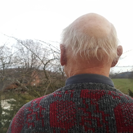 Ein älterer Mann von hinten. Er schaut in die Landschaft.