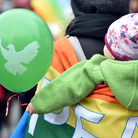 Ein kleines Kind hält während eines Ostermarsches einen Luftballon mit einer Friedenstaube fest.