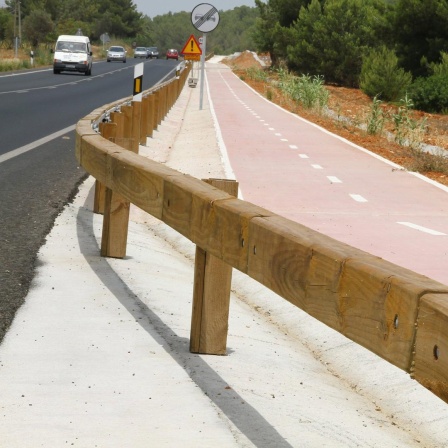 Eine Straße mit Pkws in Spanien. Straße und Radweg sind durch hölzerne Leitplanken getrennt.