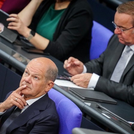 Bundeskanzler Olaf Scholz (SPD) und Bundesverteidigungsminister Boris Pistorius (SPD), sitzen im Bundestag. Pistorius schaut in sein Handy, Scholz schaut nachdenklich nach oben.