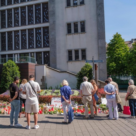 Menschen in Trauer und Gedenken stehen vor Blumen und Kerzen an der Stadtkirche in der Solinger Innenstadt