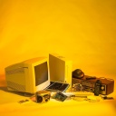 Elektroschrott wie ein alter PC und alte Handys vor gelben Hintergrund.