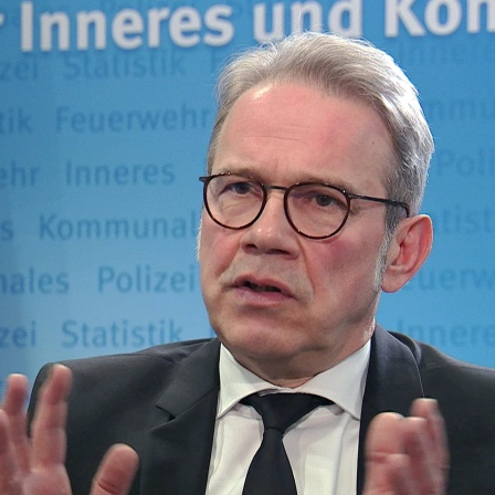 Ein Mann gestikuliert mit den Händen vor einer Thüringer Fahne.