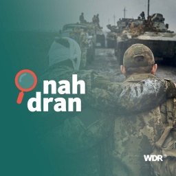 Zwei ukrainische Soldaten stehen Arm in Arm auf einem Feld. Der eine hat einen Verband um den Kopf, der andere stützt ihn. Im Hintergrund ein Konvoi von ukrainischen Militärfahrzeugen.