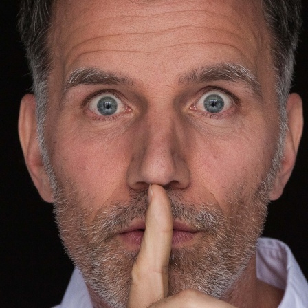 Symbolbild: Ein Mann hält sich den Zeigefinger vor den Mund.