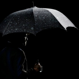 Ein schwarz gekleideter Mann trägt einen schwarzen Regenschirm auf dem Wassertropfen abperlen.