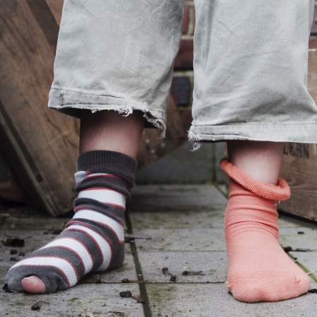 Ein Kind steht in abgetragener Kleidung ohne Schuhe und mit zwei verschiedenen Socken in einem Hinterhof