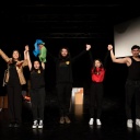 Fünf junge Mitglieder der Theatergruppe stehen mit erhobenen Armen jubelnd auf der Bühne.