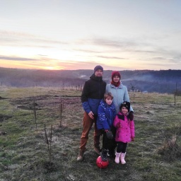 Mary (r.h.) und Yarik (l.h.) aus der zentralukrainischen Stadt Winnyzja stehen mit ihren beiden Kindern auf einer Wiese, im Hintergrund geht die Sonne unter. 
