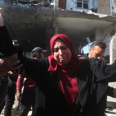 Eine Palästinenserin reißt verzweifelt vor zerbombten Gebäuden die Hände in die Höhe.