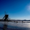 Schlittschuhläufer auf zugefrorenen Kanälen neben einer Windmühle in den Niederlanden