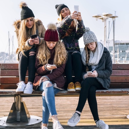 Vier junge Mädchen sitzen auf einer Bank und spielen mit ihrem Handys.