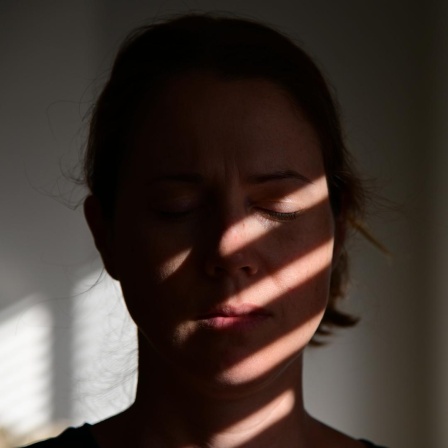 Porträt einer Frau mit geschlossenen Augen, auf deren Gesicht sich die Schatten einer Jalousie abzeichnen.