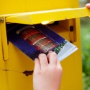 Eine Kinderhand steckt eine Postkarte in einen Briefkasten