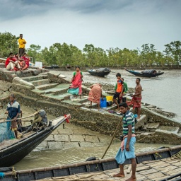 An einem indischen Flussufer sind buntgekleidete Menschen mit ihren Booten zu sehen.