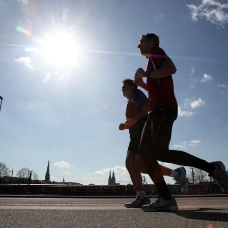 Jogger laufen bei direkter Sonneneinstrahlung auf einem Weg.
