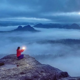 Sitzende Frau auf einer Bergspitze mit Licht in der Hand.