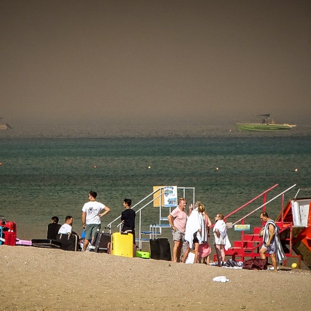 Touristen stehen an einem Strand, wohin sie wegen eines Waldbrandes auf der griechischen Insel Rhodos in Sicherheit gebracht worden sind.