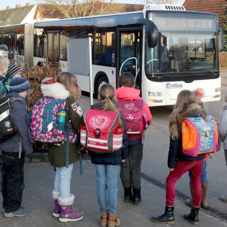 Kinder stehen vor einem Schulbus, bereit zum Einsteigen.