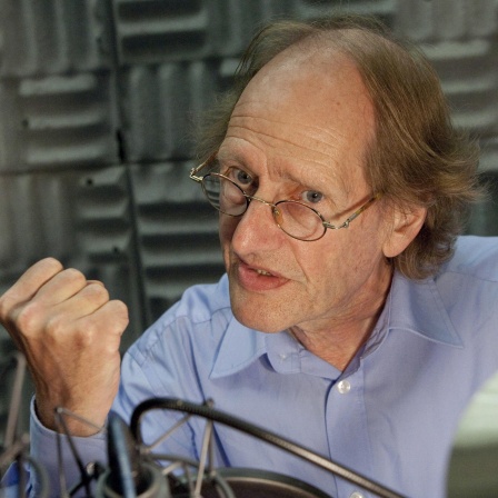 Ein Mann mit schütterem Haar und Brille gestikuliert in einem Hörfunkstudio mit der Faust vor dem Mikrofon