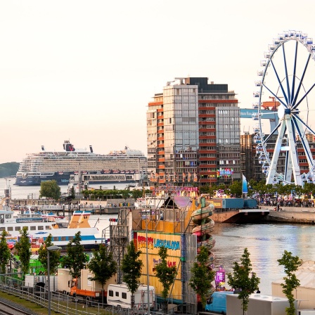 Ein Riesenrad dreht sich bei der Kieler Woche 2024. Im Hintergrund fährt das Kreuzfahrtschiff "Mein Schiff 7".