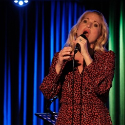 Eine Frau steht auf einer Bühne und singt in ein Mikrofon.